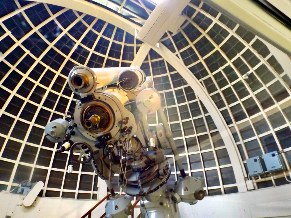 Auto-generated description: A large telescope is positioned inside an observatory with a domed, windowed ceiling.