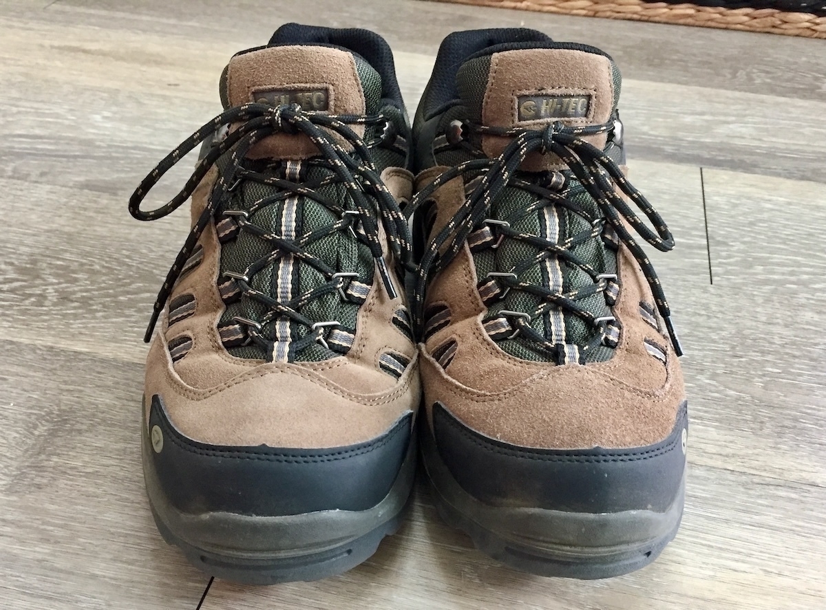 Auto-generated description: A pair of brown and black hiking boots with green accents is placed on a wooden floor.