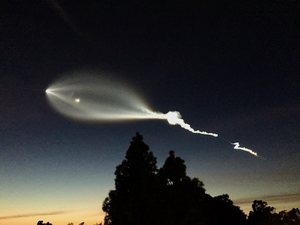 Auto-generated description: A glowing streak of light trails across the twilight sky, resembling a rocket launch or celestial event.
