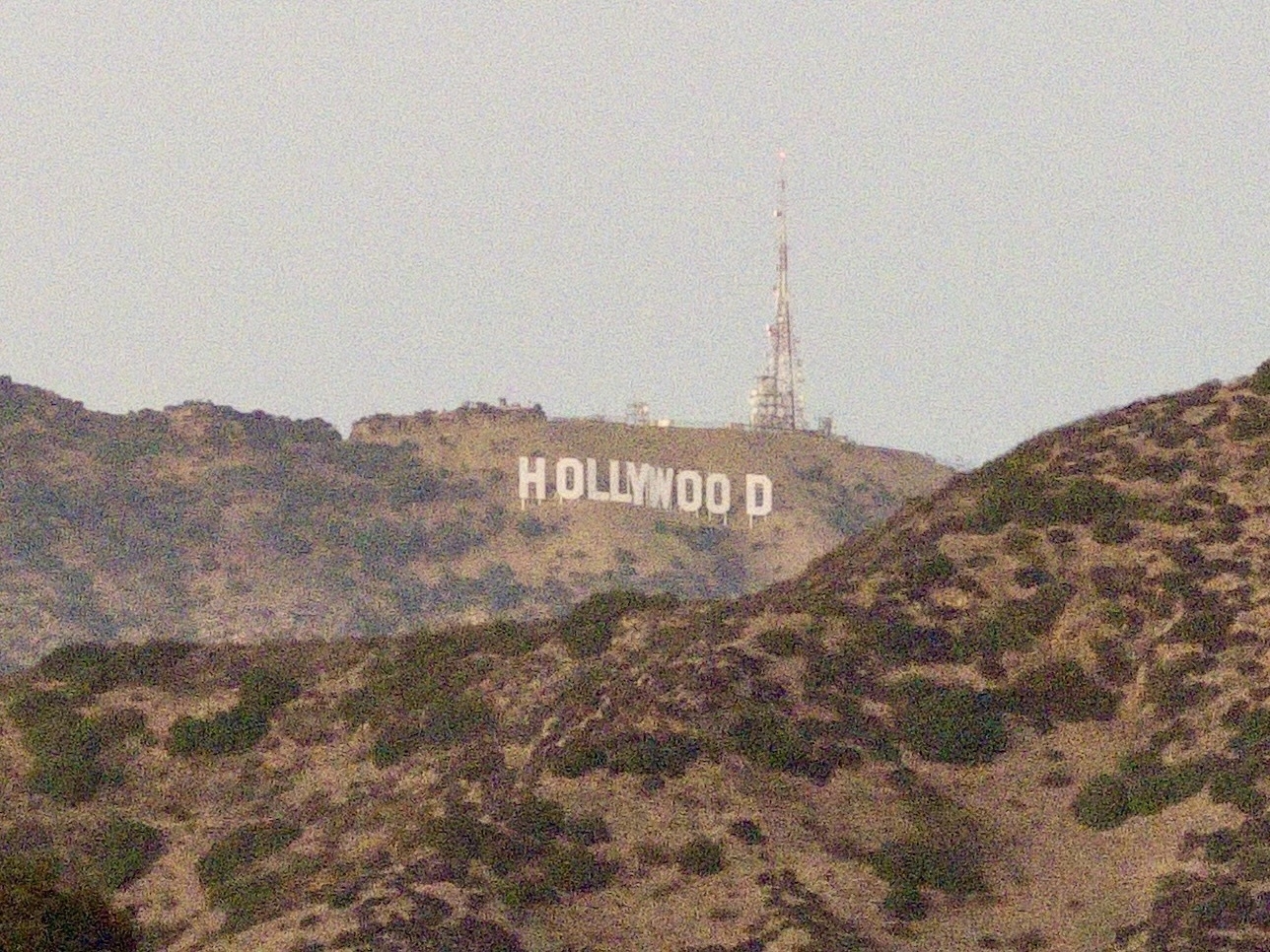 Large white letters spelling 'HOLLYWOOD' are situated on a hillside with rugged terrain in the foreground.