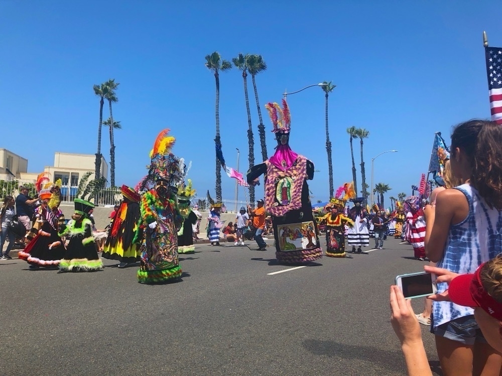 Cultural dancers in a parade as the crowd looks on.
