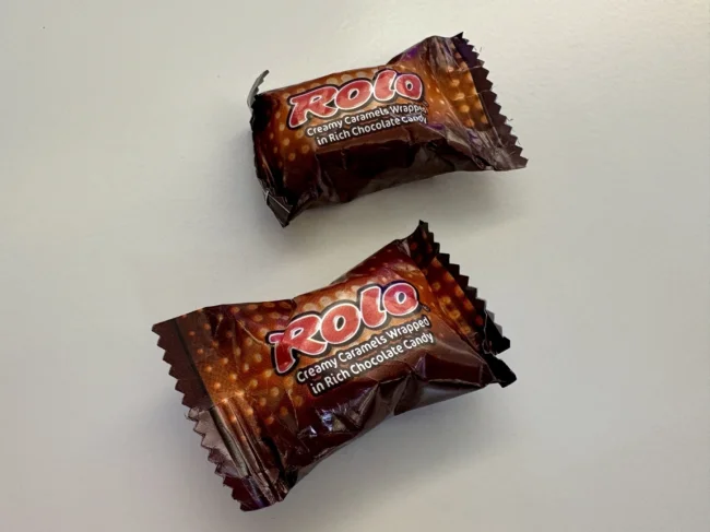 Auto-generated description: Two individually wrapped Rolo creamy caramel chocolate candies are placed on a light-colored surface.