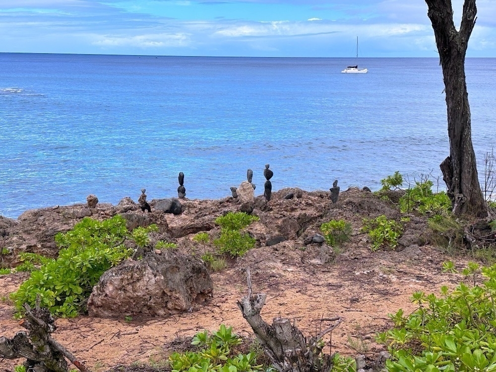Rocks stacked on a shoreline with a sailboat in the background.